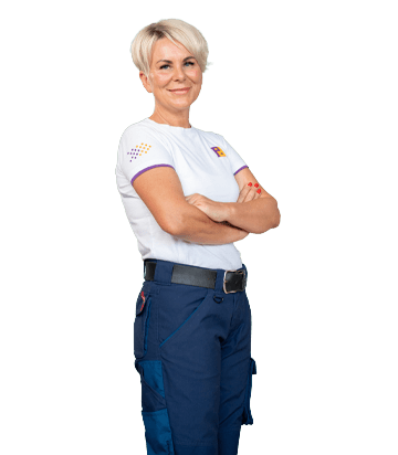 Frau in blauer Arbeitshose und weißem T-Shirt schaut mit verschränkten Armen lächelnd in die Kamera.